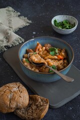 Tripas - pork tripe stew with white beans and smoked sausages in a blue bowl on the dark table