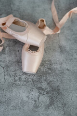 A pair of pink ballet slippers isolated on a gray surface, in vertical image. - obrazy, fototapety, plakaty
