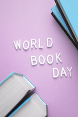 A stack of books in shades of electric blue, purple, and magenta with World Book Day written in violet font on the top book, all in a rectangular shape - obrazy, fototapety, plakaty