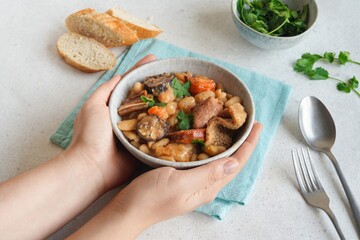 Female hands holding a bowl with Portuguese tripas - Tripe stew on the white table. Traditional gastronomy concept. - obrazy, fototapety, plakaty