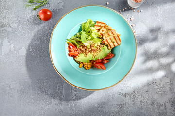 Top view of a grilled chicken and avocado salad bowl with vegetables, served on a textured surface