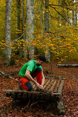 man builds a handcrafted boat with wooden logs in the middle of an autumn forest of beech trees...