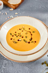 Velvety Pumpkin Soup Garnished with Pepitas and Olive Oil on a Rustic Ceramic Plate