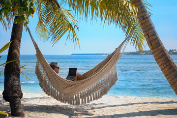 man working on laptop computer while relaxing in beach hammock, freelance worker, remote job via internet - 788216745
