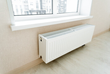 The radiator of the battery hangs on the wall under the window.