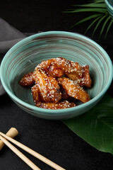 Roasted chicken wings in teriyaki sauce with sesame on ceramic bowl. Buffalo wings in asian style on black concrete background. Aesthetic composition with fried chicken wings, chopsticks and leaf. - 788218529