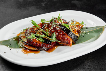 Delicatessen appetizer - grilled octopus with eggplant in teriyaki sauce. Boiled octopus tentacle and vegetables in pan asian style. Salad with octopus and eggplant in miso sauce on black table. - 788218905