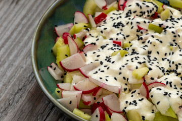 Close up view of a bowl with homemade red radish and cucumber salad with yogurt dressing and nigella seeds. 