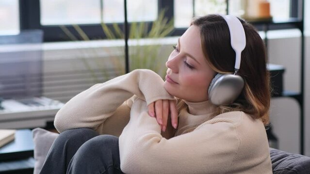 Happy Caucasian woman in wireless headphones listening music at home. Spending weekend leisure time, enjoying audio entertainment.