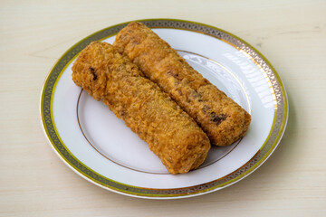 Chicken spring rolls on white plate on wooden background. They are made with a crispy pastry and a flavorful chicken filling seasoned with herbs and spices. 