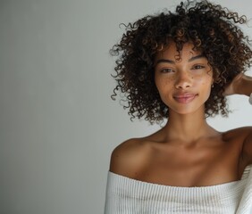  A beautiful mixed race model with curly hair, smiling and posing in front of the camera wearing a denim vest top, hands behind her head against a white background in a studio photography setting with