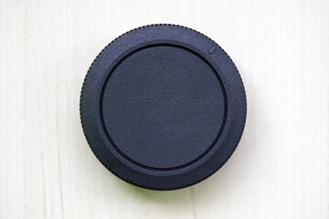 Camera lens cover or lens dust cap without logo on wooden textured white background. A lens cover or lens cap protects camera lenses from scratches, dust, rain, snow, and minor collisions.