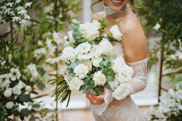 A happy bride in a wedding dress holds a bouquet of white flowers