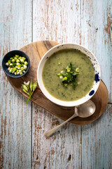 Bowl of wild garlic soup served on a wooden board with garnish of wild garlic flowers and spring onions