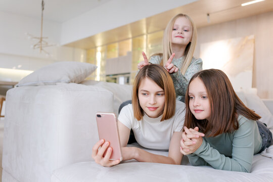 Three girls are laying on couch, one of them holding a cell phone