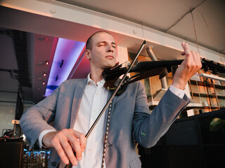 Musician in business attire playing an electronic violin with intense focus.