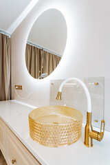 A bathroom with a round mirror, gold sink, and wood accents for added comfort