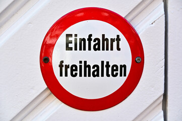 Rundes Verkehrschild oder Verkehrszeichen mit der Aufschrift "Einfahrt freihalten" in deutscher Sprache auf weißem Grund mit rotem Rand und zwei Nägeln