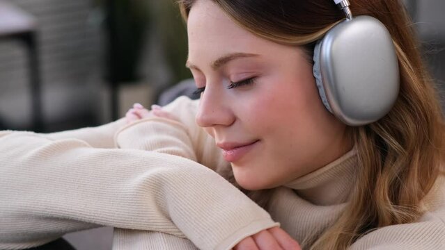 Close up portrait of a serene Caucasian young woman listening music during leisure time, using headphones at home. Enjoying entertainment on weekend.