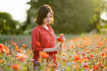 Beautiful teenage girl admiring poppy and knapweed flowers in blossoming poppy field on sunny...