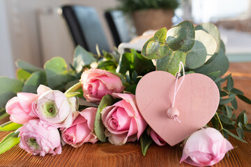 Bouquet of pink roses with ranunculus and pink heart shape on wooden table for mother's day greetings.