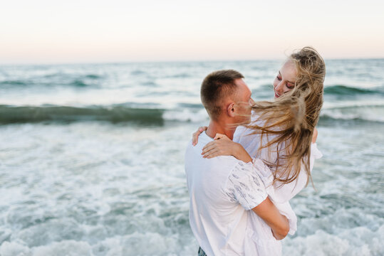 Happy people spend time together. Couple in love hugging on seashore in sea. Male hugs female standing on water with big waves ocean and enjoying summer day. Man embraces woman walk on beach sand sea.