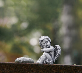 Kleiner sitzender Engel auf Stein vor soften Hintergrund