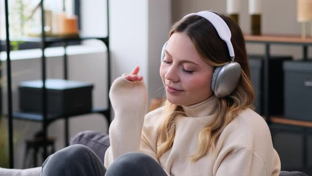 Portrait of a friendly and relaxed Caucasian young woman resting on sofa and listening music in headphones at home. Spending leisure time on weekend.