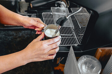 Close-up of Barista hand using high-pressure steam-operated milk frother to prepare a cappuccino and latte coffee milk