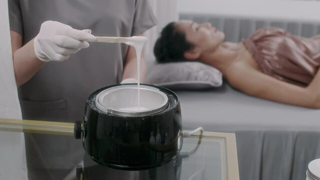 Cropped shot of unrecognizable specialist melting and mixing wax with spatula for hair removal procedure in spa salon