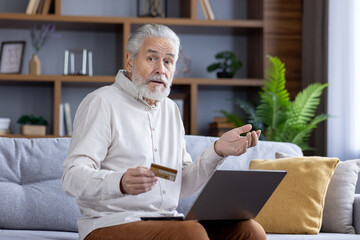 Senior man holding credit card, looking puzzled on couch