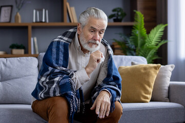Thoughtful senior man at home wrapped in cozy blanket