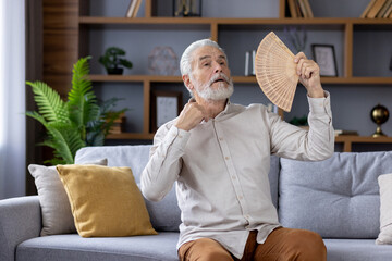 Senior man feeling hot and using fan on warm day at home