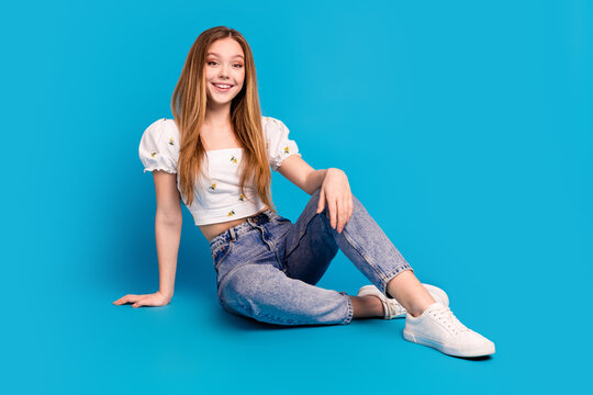 Full size photo of nice young girl sit posing floor wear top isolated on blue color background