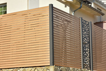 Naturbelassener Holzplankenzaun mit beschichteten Stahlpfosten und Naturstein-Gabionen sowie Natursteinmauer als Abgrenzung und Sichtschutz für die Terrasse eines Wohnhauses © Hermann