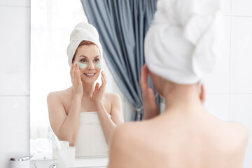 Woman wrapped in towel is examining her face in mirror, focusing on her skin, lips, eyebrows. She...