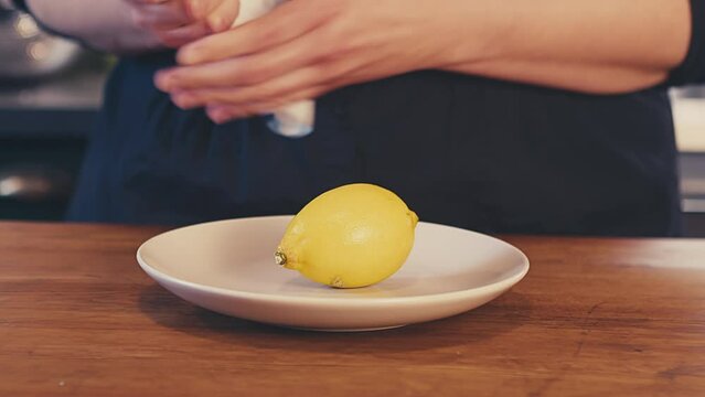 Close up of woman's hands cleaning, and wiping dry a whole fresh lemon with paper towel. Defocused brightly lit kitchen in the background. Studio shot. . High quality 4k footage