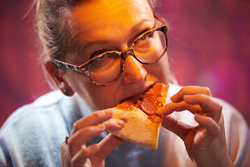 45 year old woman with glasses eats pizza