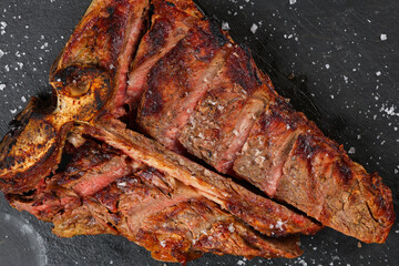 T-bone steak. Close up photo with a beef t-bone steak on a black platter with spread salt around...