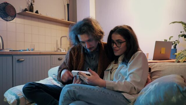 Intimate couple engrossed in smartphone together, cozy home atmosphere.