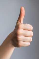 Close-up of a thumb up gesture, clear skin, neutral soft grey background, symbol of approval and positivity