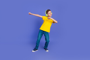 Fototapeta na wymiar Photo of glad positive boy wear trendy yellow clothes have fun listen music look empty space isolated on purple color background