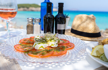Caprese style salad of mozzarella and tomato with basil dressing with rosé wine at beach club on...