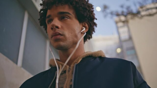 Mixedrace guy listening song in earphones strolling city closeup. Curly teenager