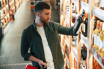 Standing near the shelf. Man is choosing wine in the store