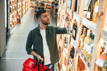 Standing near the shelf. Man is choosing wine in the store