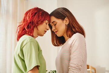 serene young lesbian couple with closed eyes standing next to each other at home, bliss and love