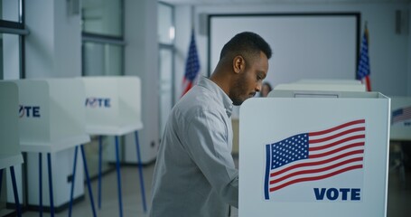 African American man takes paper ballot for voting from polling officer at polling station. US...