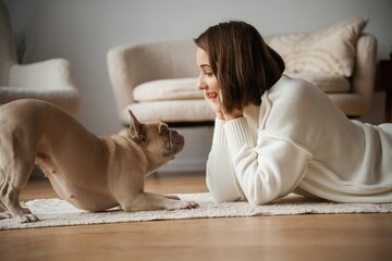 View from the side, lying down on the floor. Young woman is with her pug dog at home