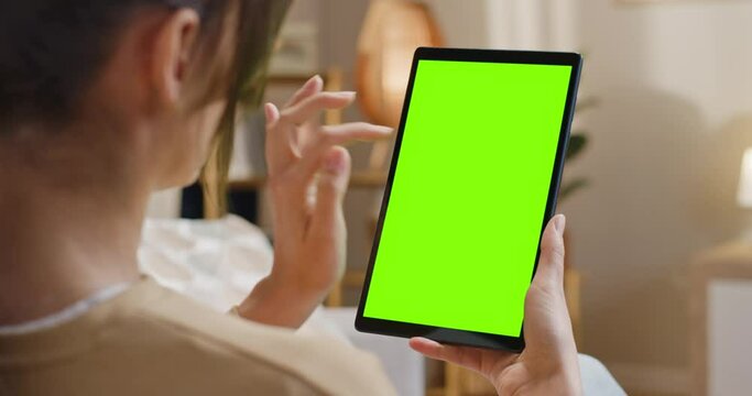 Close up view of woman working with tablet at well designed home. Female scrolling mock up screen. Woman using device with chroma key screen. Female looking at green template display.